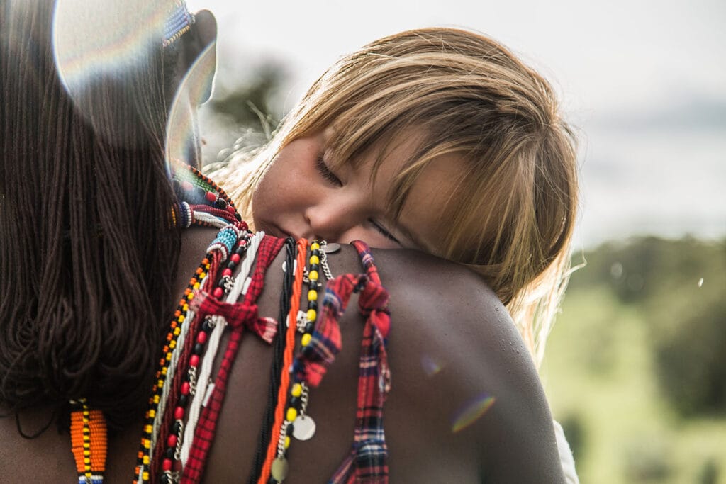 Kid falling asleep on a maasai warrior shoulders while on a family safari in Kenya